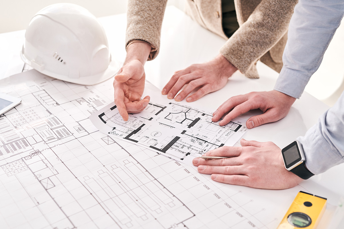 Close-up of unrecognizable architects standing at desk and working with house plan in office